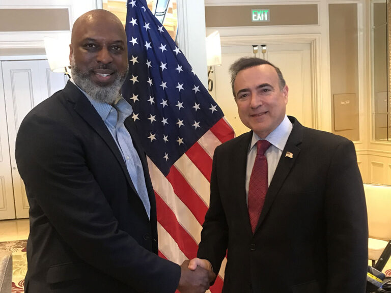 2 men shaking hands with American flag on background