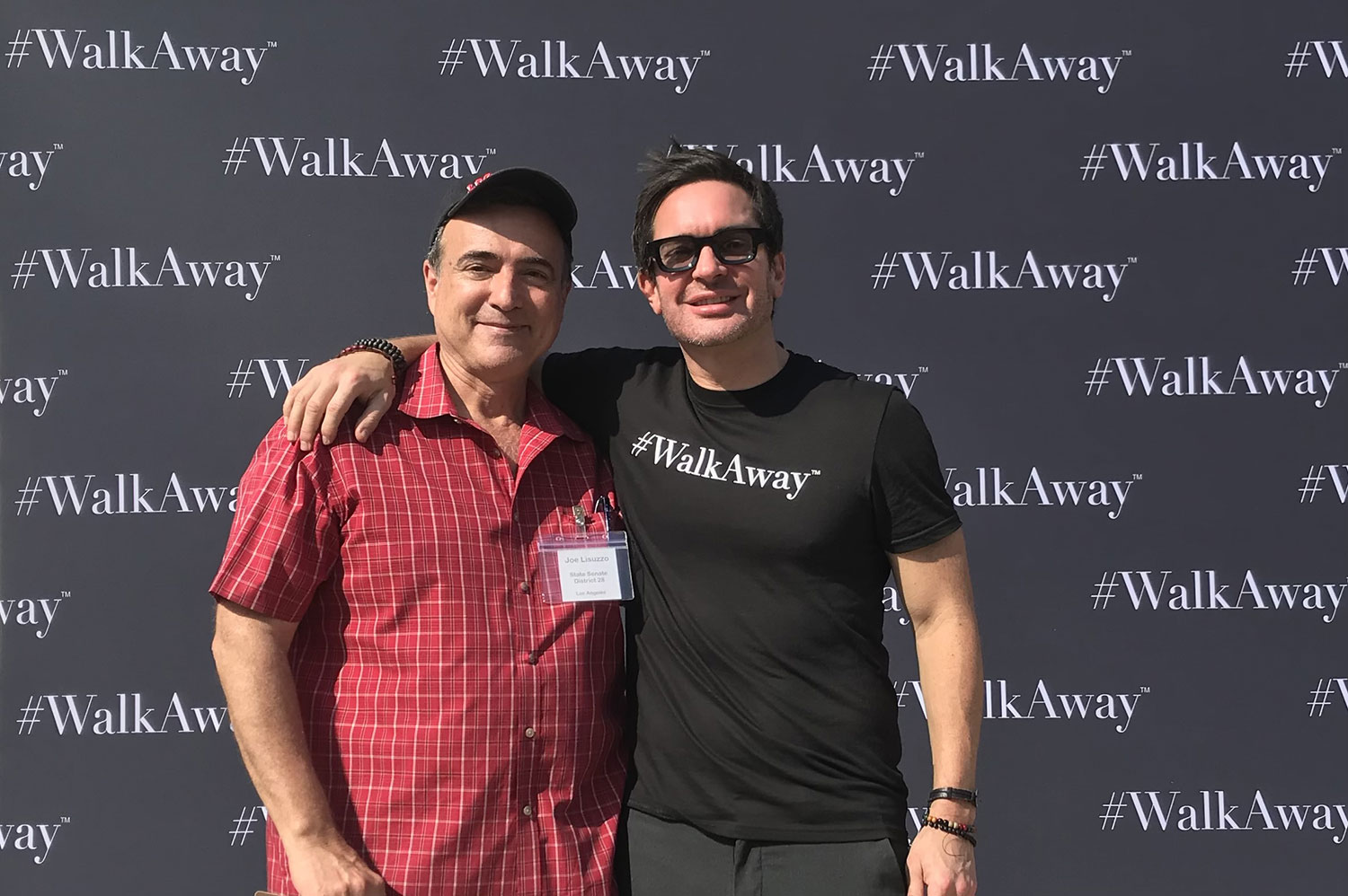a man in black shirt with arms in the shoulder of the man with cap